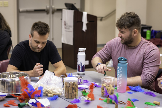 Two volunteers create at toys out of pipe cleaners, feathers, and cork.