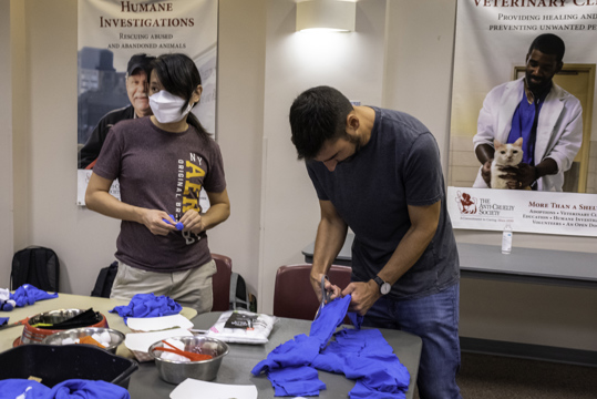 Two volunteers cut up old t-shirts to create toys with